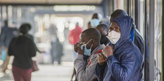 People wearing protective face masks wait for a bus Johannesburg, South Africa. Photographer: Waldo Swiegers/Bloomberg