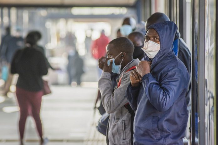 People wearing protective face masks wait for a bus Johannesburg, South Africa. Photographer: Waldo Swiegers/Bloomberg